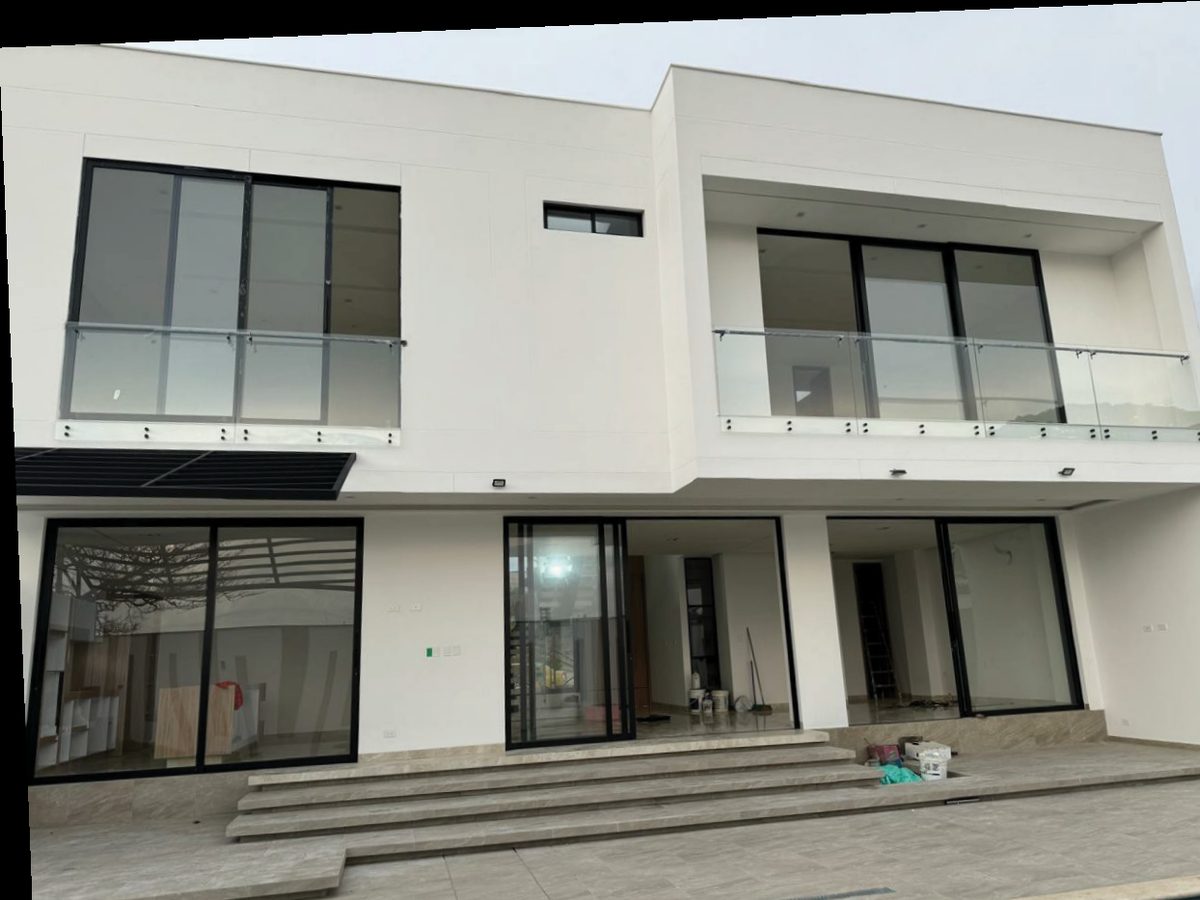 Casa moderna de dos pisos con ventanería en aluminio y barandas de vidrio